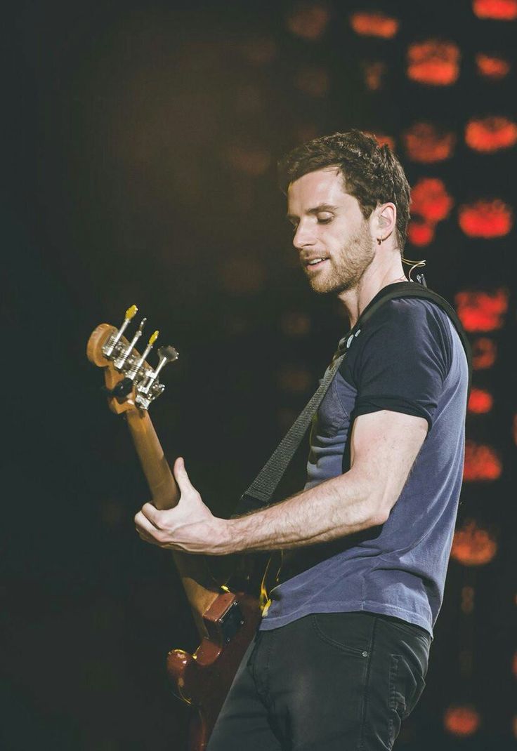 a man holding a guitar while standing on top of a stage with lights in the background