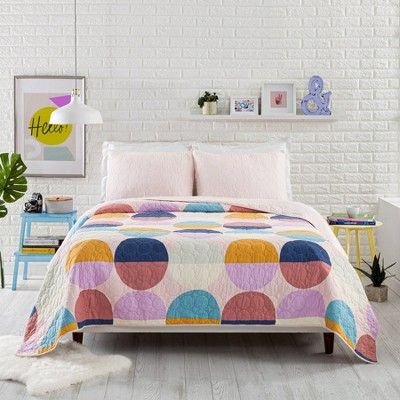 a bedroom with white brick walls and a bed covered in a colorful polka dot quilt