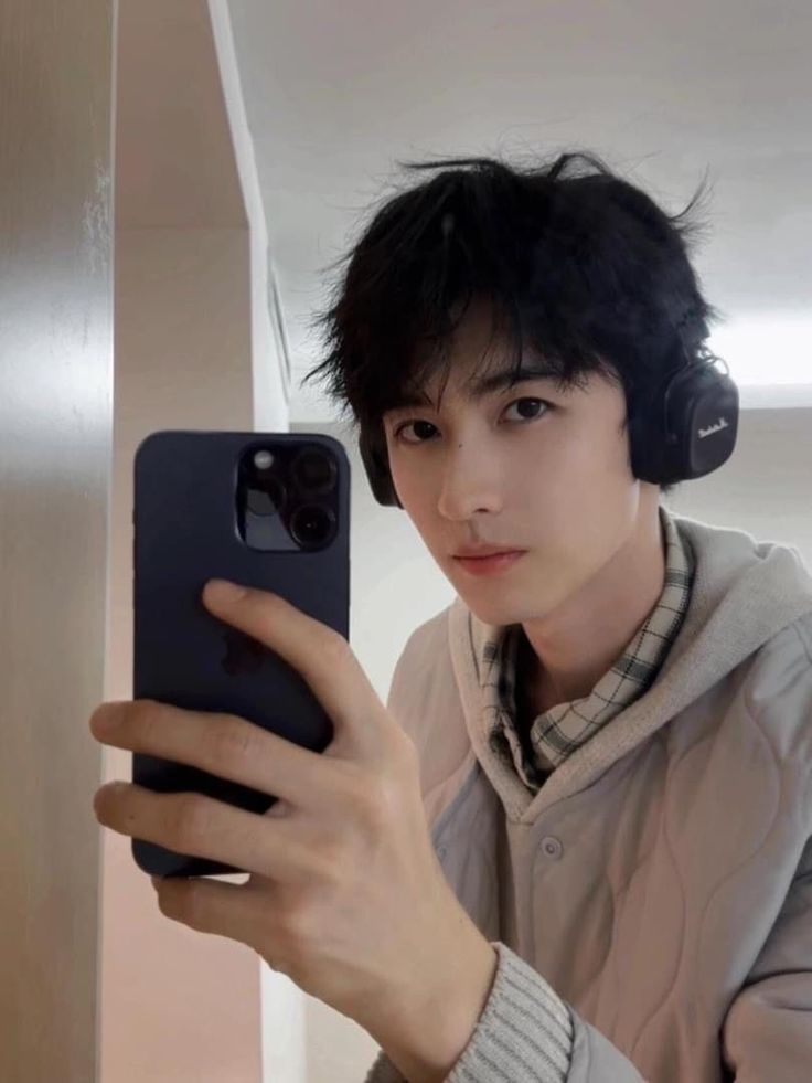 a young man wearing headphones is taking a selfie with his cell phone in front of him