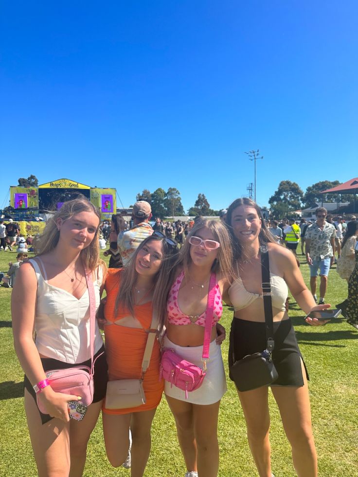 three girls in bathing suits posing for the camera at a music festival with other people