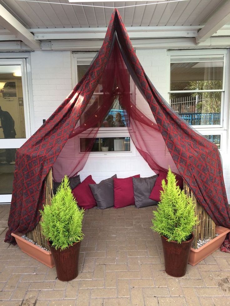 two potted plants sitting under a canopy on a patio with red curtains over it