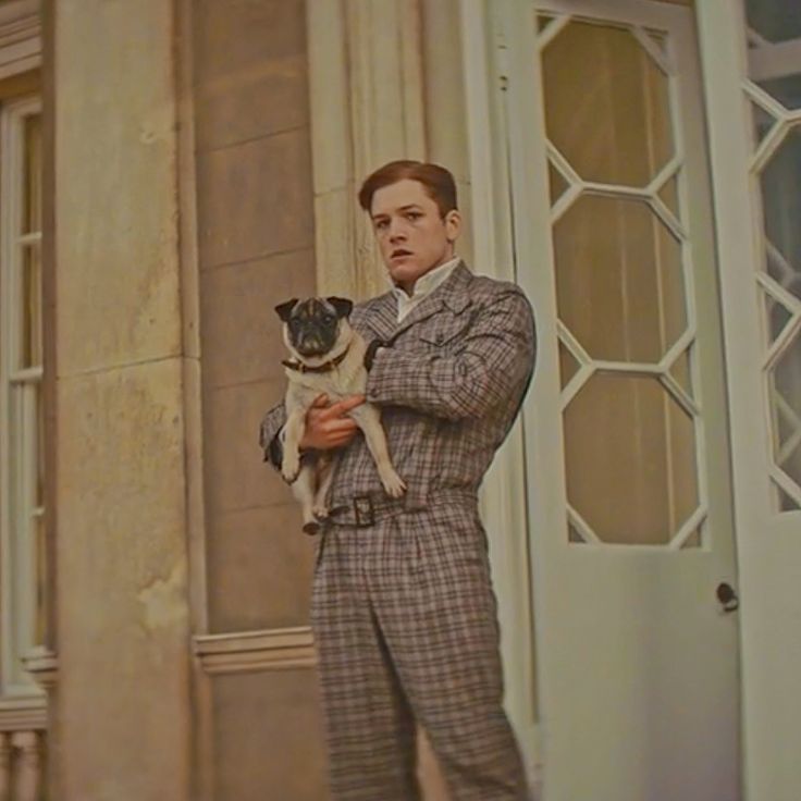 a man holding a small pug dog in front of a building with white doors