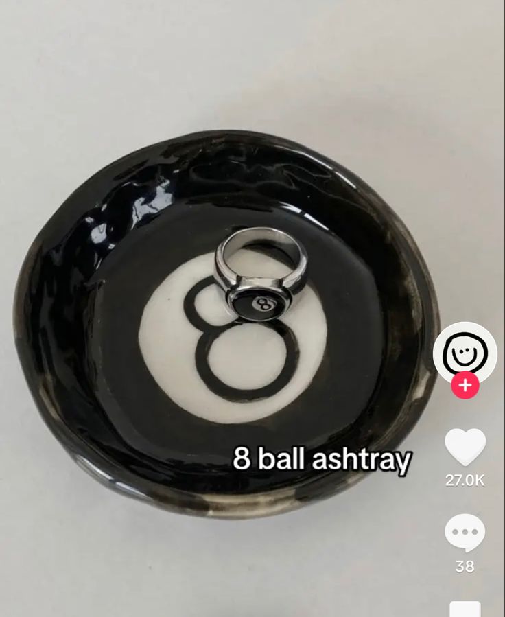 a black and white bowl with two wedding rings on the bottom that says 8 ball ashtray