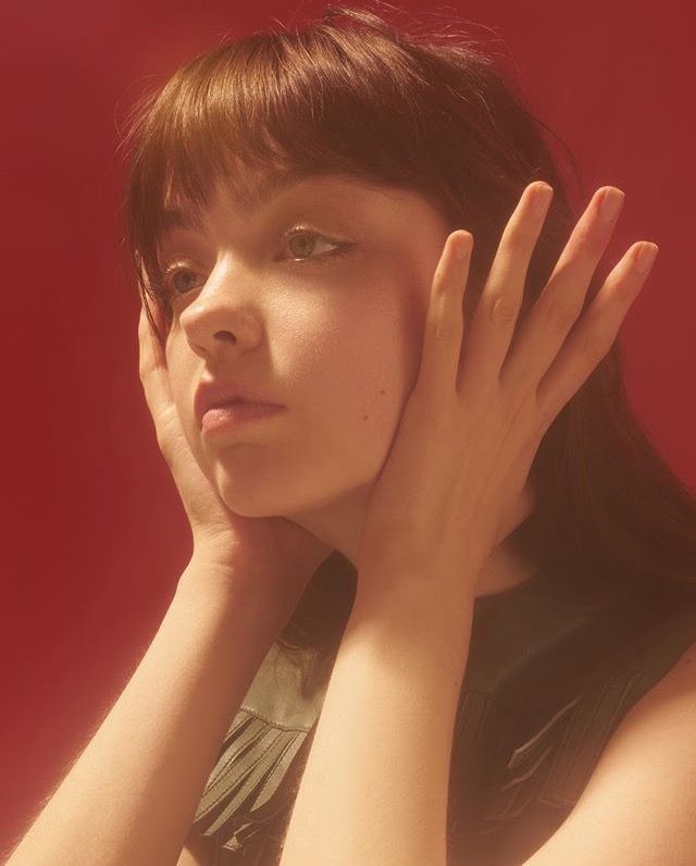 a woman is posing with her hands on her face and looking off to the side