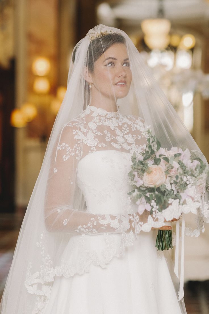 a woman in a wedding dress holding a bouquet and looking at the camera while wearing a veil