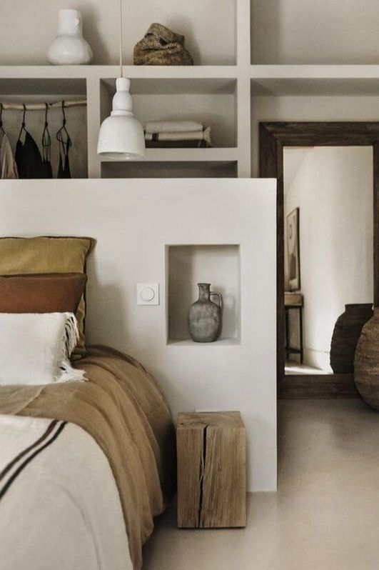 a bed sitting in a bedroom next to a wooden shelf filled with books and vases