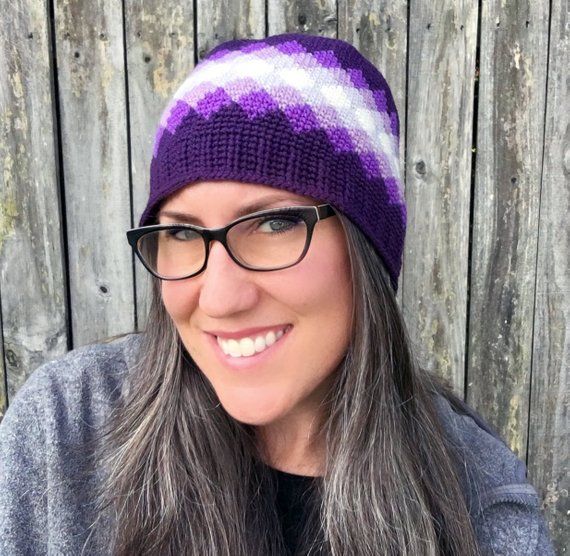 a woman with glasses wearing a purple and white knitted hat, smiling at the camera