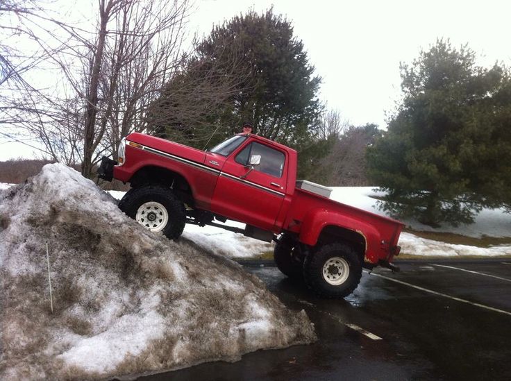 a red pick up truck parked on top of a pile of snow next to trees