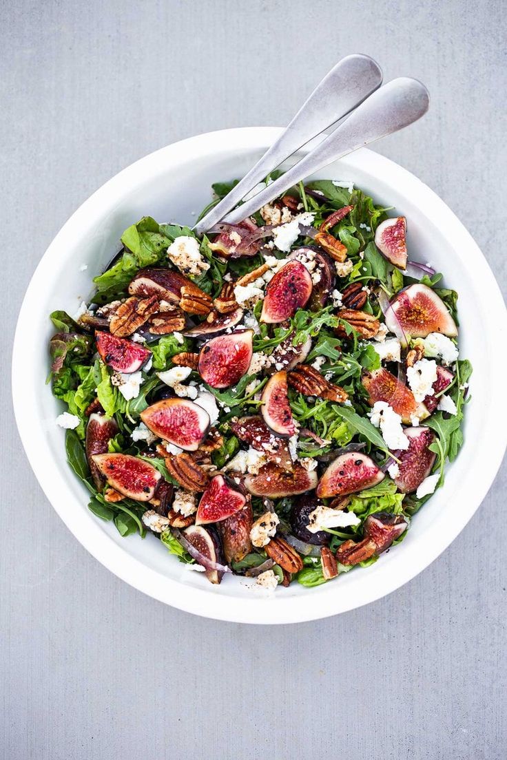 a white bowl filled with salad topped with figs and goat cheese next to a fork