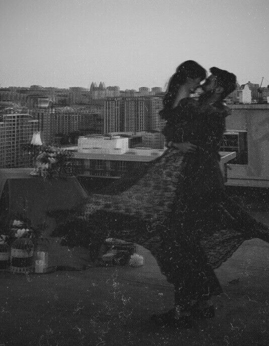 a woman standing on top of a roof next to a tall building with buildings in the background