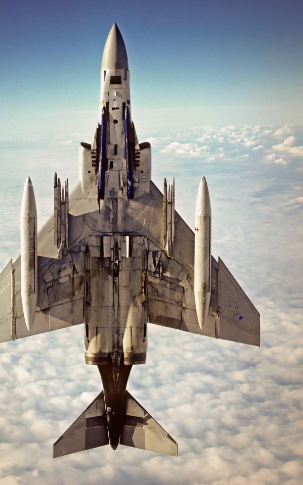 a fighter jet flying through the air above clouds and blue sky with no one around it