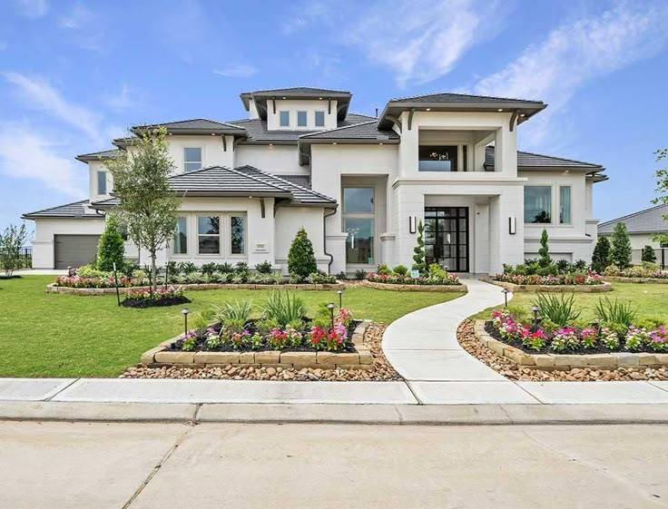 a large white house with lots of flowers in the front yard and landscaping around it