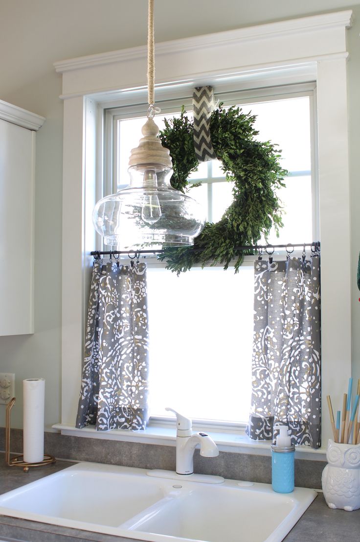 a kitchen sink under a window with a wreath hanging from the window sill above it