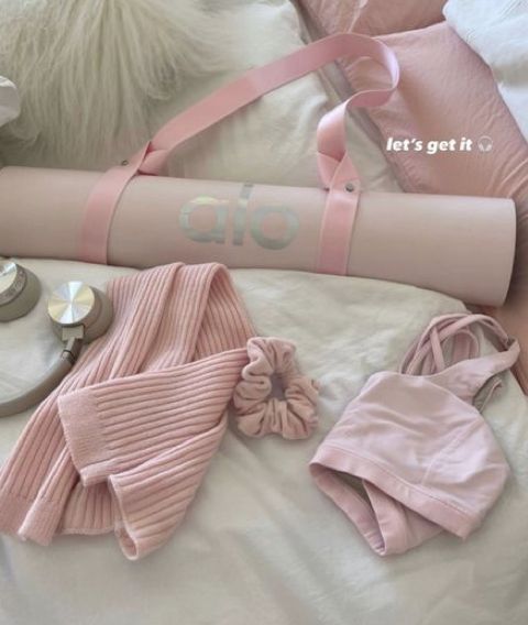 pink items are laying on a bed with white sheets and pillows, such as a handbag