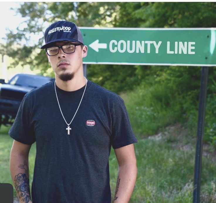 a man standing in front of a street sign that says county line and has a cross on it