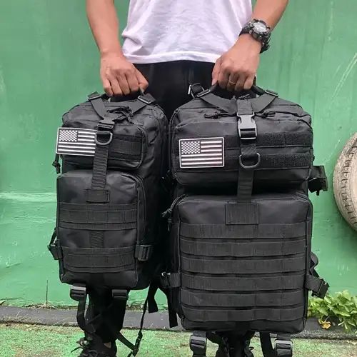 two men standing next to each other in front of a green wall holding black backpacks