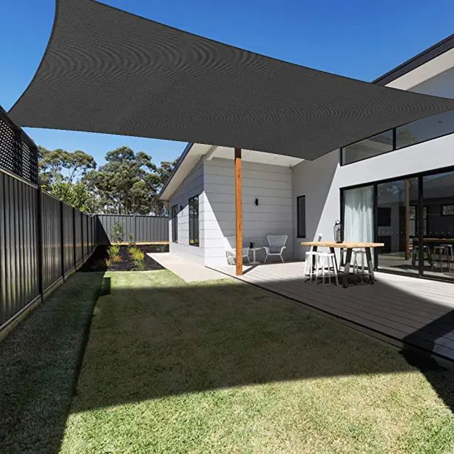 an outdoor area with grass, table and chairs under a large shade sail over the patio