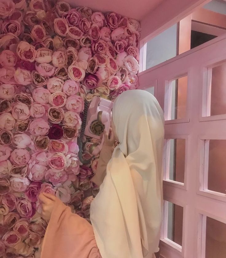 a woman wearing a hijab is looking at flowers on the wall behind her