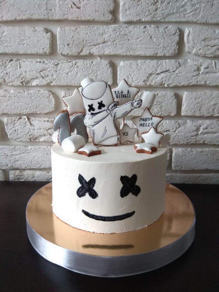 a cake decorated with white frosting and black decorations is on a plate next to a brick wall