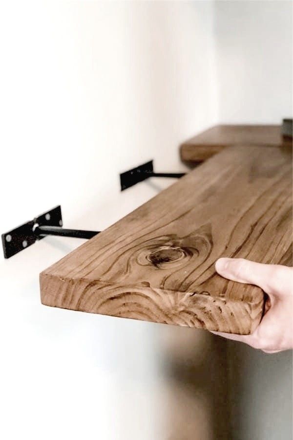 a hand is holding the edge of a wooden table with two black brackets on it