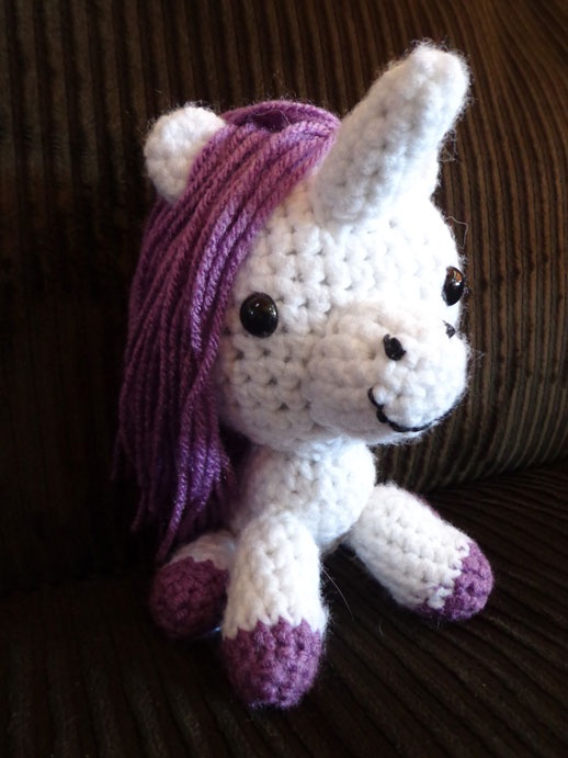 a crocheted white and purple stuffed animal sitting on a couch with its hair blowing in the wind