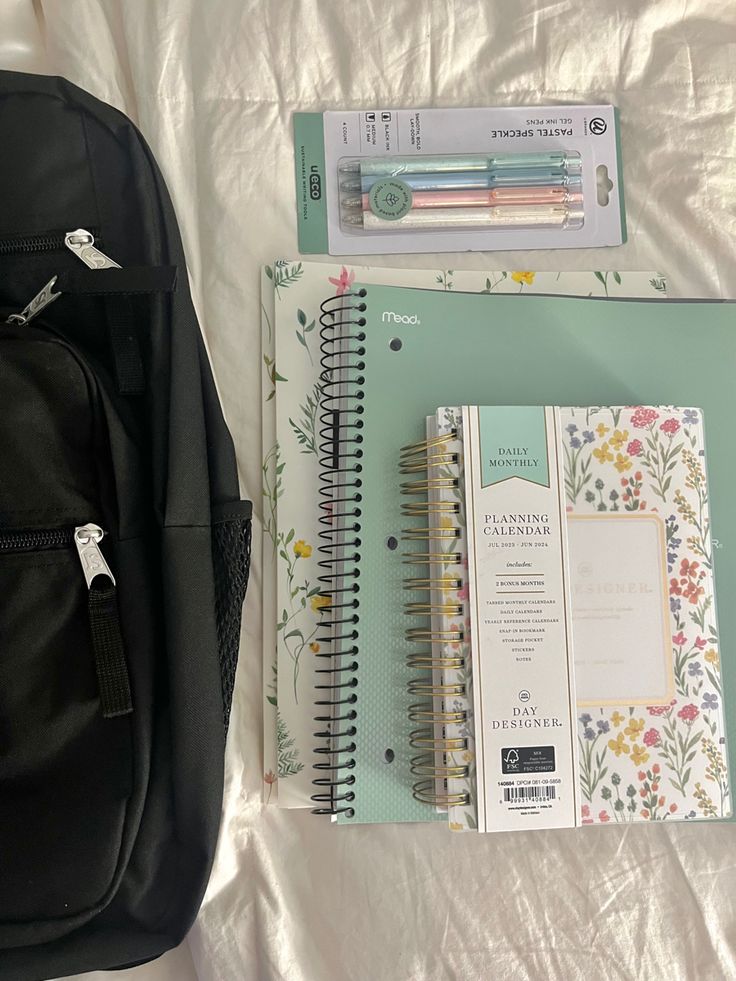 a backpack, notebook and pen sitting on top of a bed next to each other