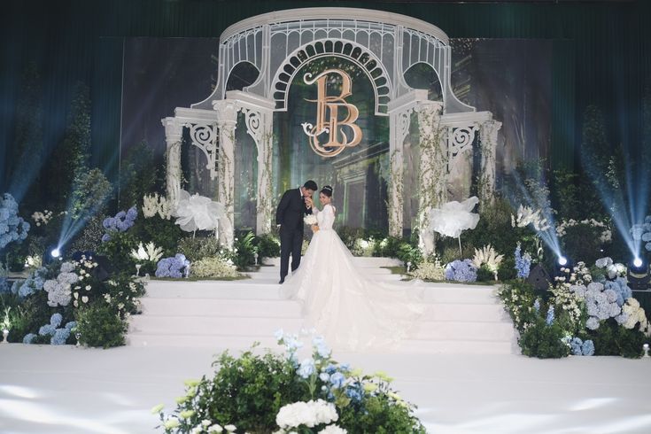 a bride and groom standing in front of a stage with blue flowers on it at their wedding