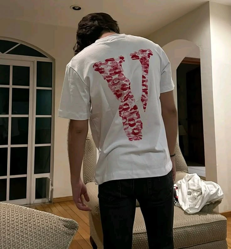 a man standing in front of a couch wearing a t - shirt with the letter v on it