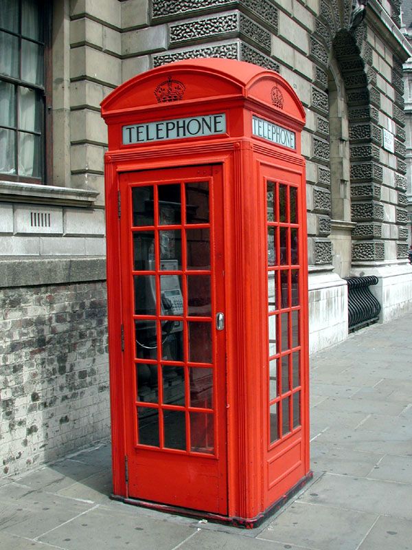 a red telephone booth sitting on the side of a street in front of a building