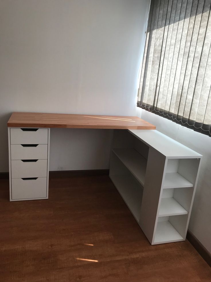 an empty room with a desk and bookcase next to a window in the corner