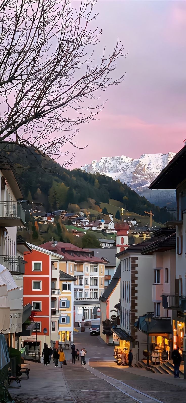 people are walking down the street in front of some buildings with mountains in the background