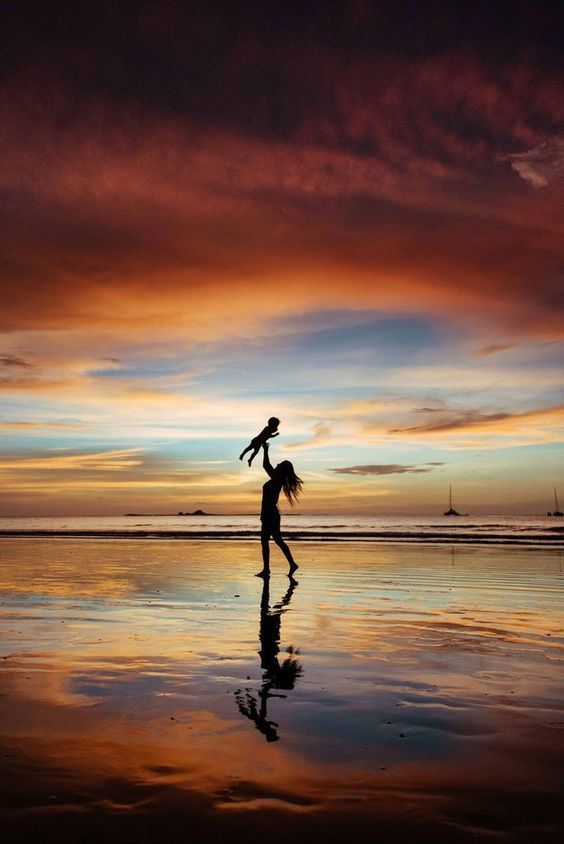 a person holding a child on the beach at sunset