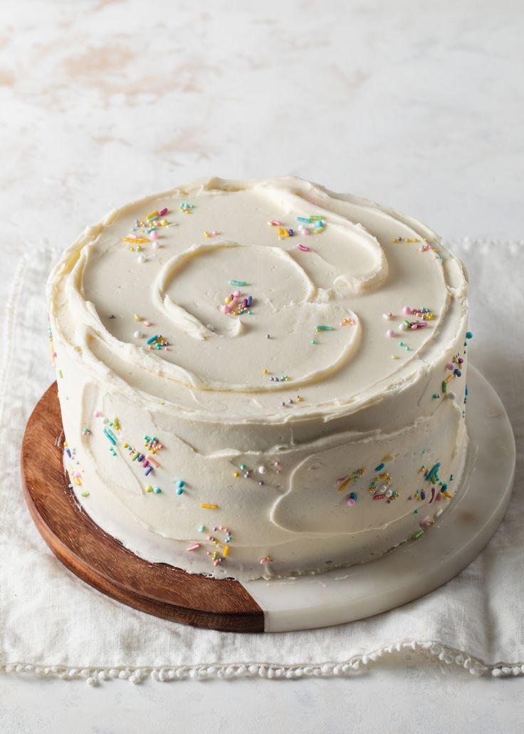 a cake with white frosting and sprinkles on a wooden platter