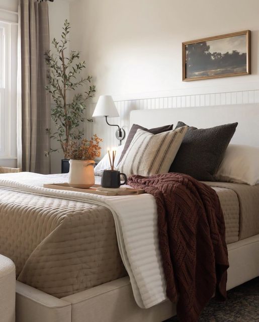 a bed with pillows and blankets on top of it next to a window in a bedroom