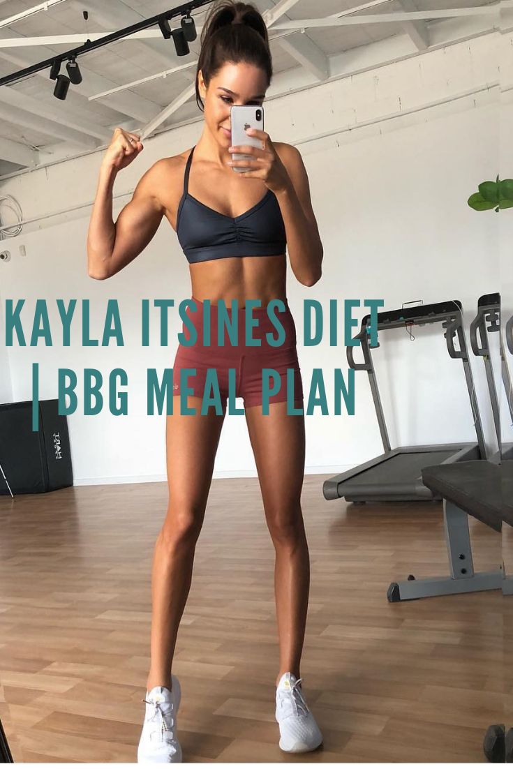 a woman taking a selfie with her cell phone in a gym room while standing on a hard wood floor