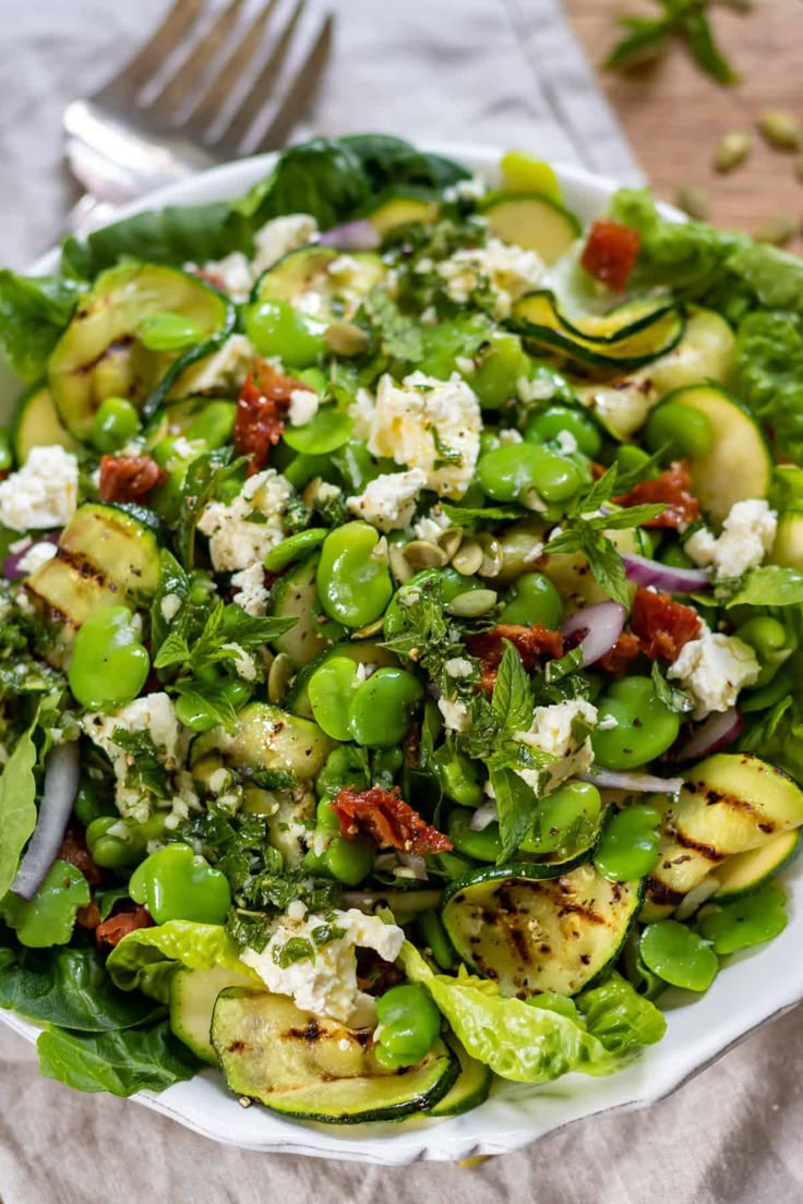 a white bowl filled with green vegetables and feta cheese on top of a table