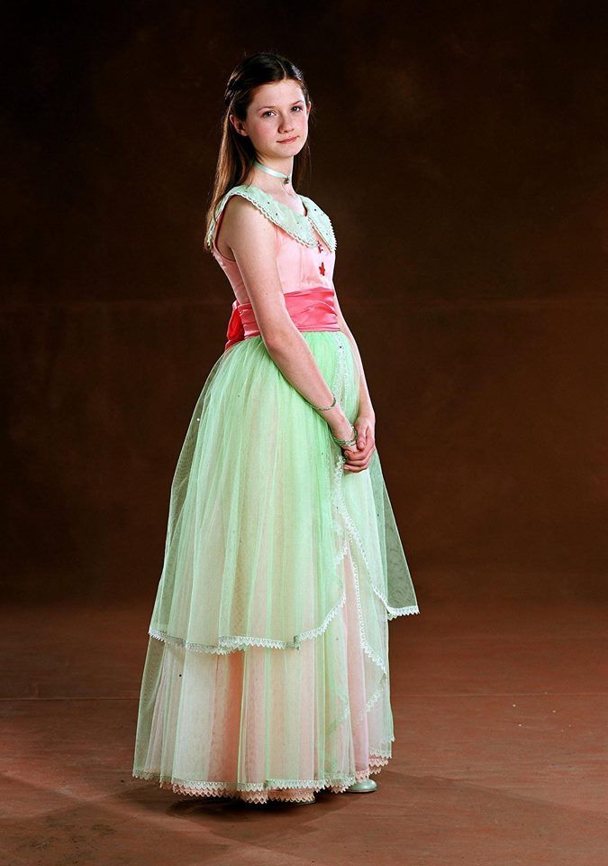 a woman in a green and pink dress standing on a brown floor with her hands behind her head