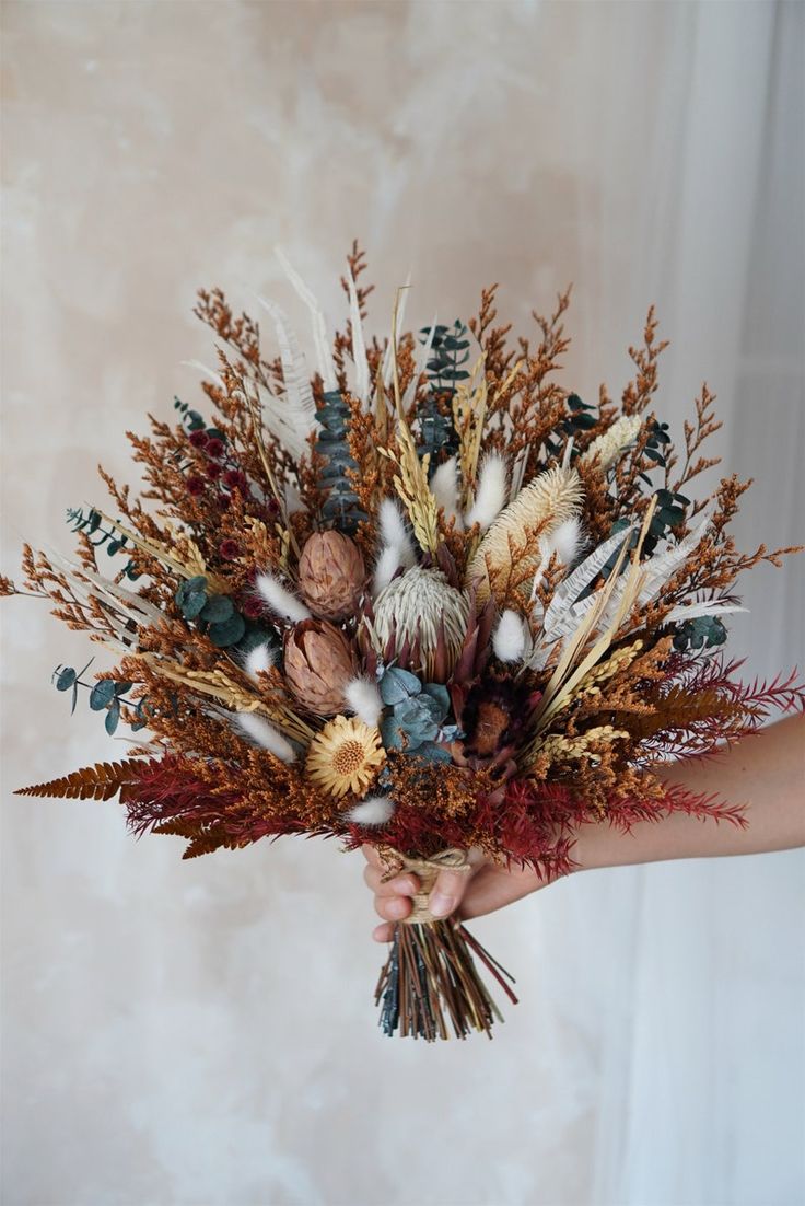 a person holding a bouquet of dried flowers