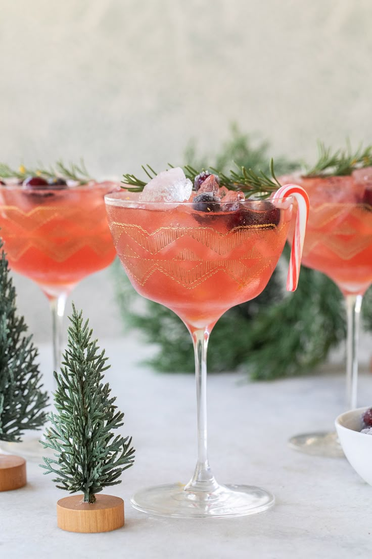 three glasses filled with pink liquid and garnished with pine needles, surrounded by evergreen branches