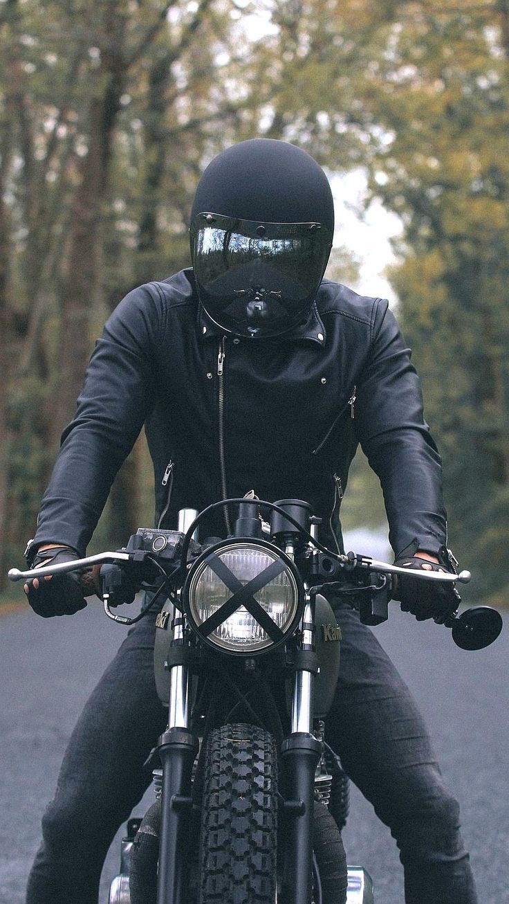 a man riding on the back of a motorcycle down a road next to some trees