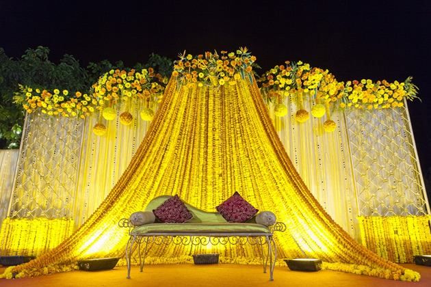 an outdoor stage decorated with flowers and yellow draping for a wedding or reception