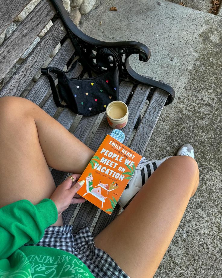 a person sitting on a bench with a book and coffee cup in front of them