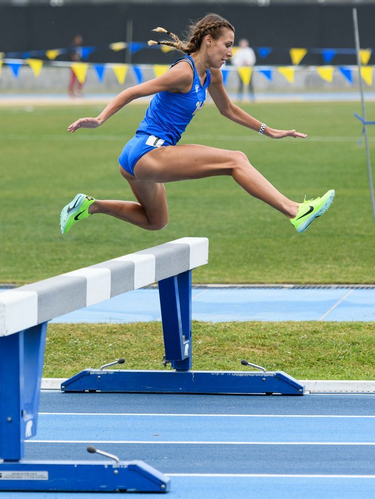 a woman jumping over a hurdle on top of a blue track