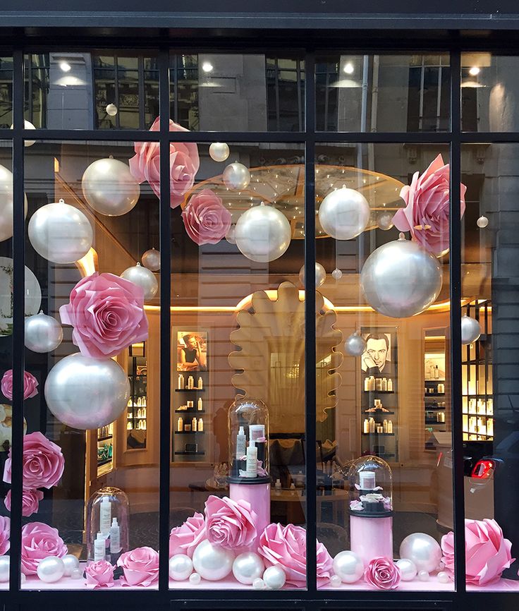 a window display with pink and white flowers in the front, and lots of balloons behind it