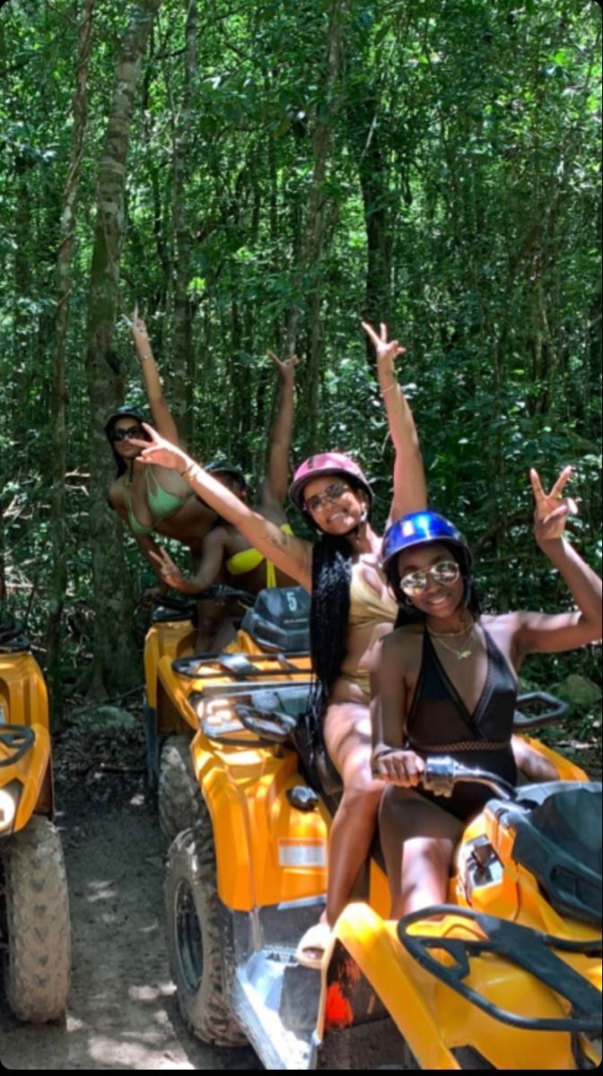 four people riding on atvs in the woods with trees behind them and one person waving