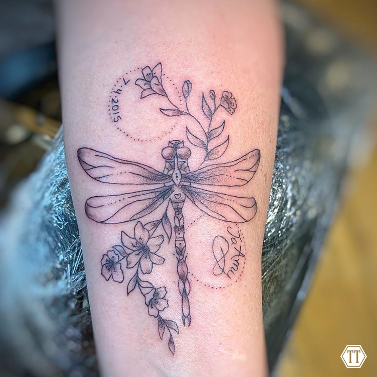 a dragonfly tattoo on the arm with flowers and leaves around it's wings