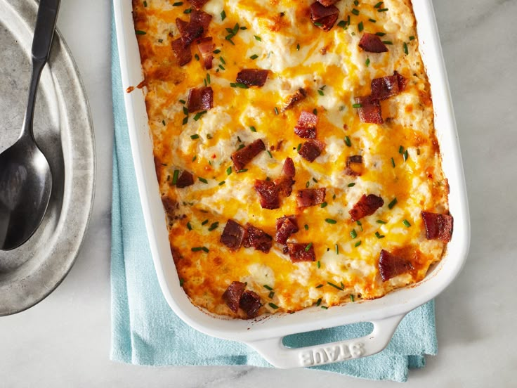 a casserole dish with cheese and bacon in it next to a serving spoon