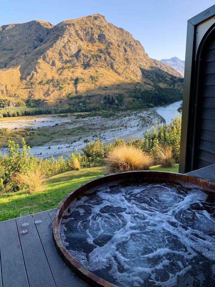 a hot tub sitting on top of a wooden deck next to a mountain range in the distance