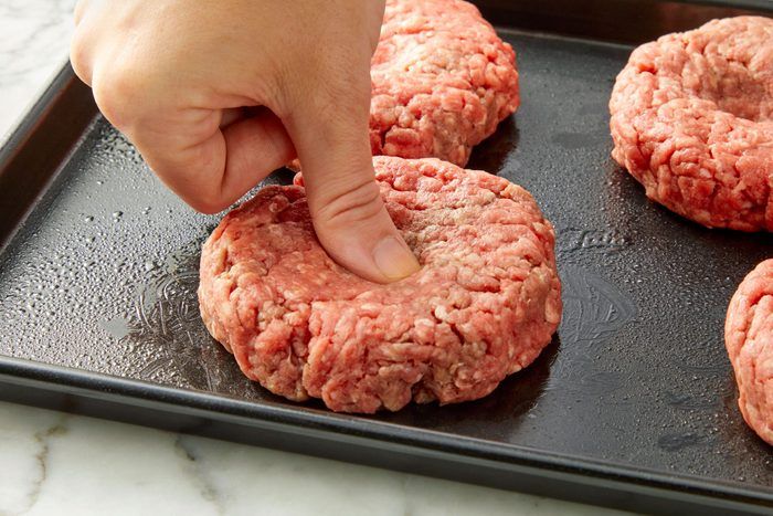 a person placing hamburger patties on top of a black tray