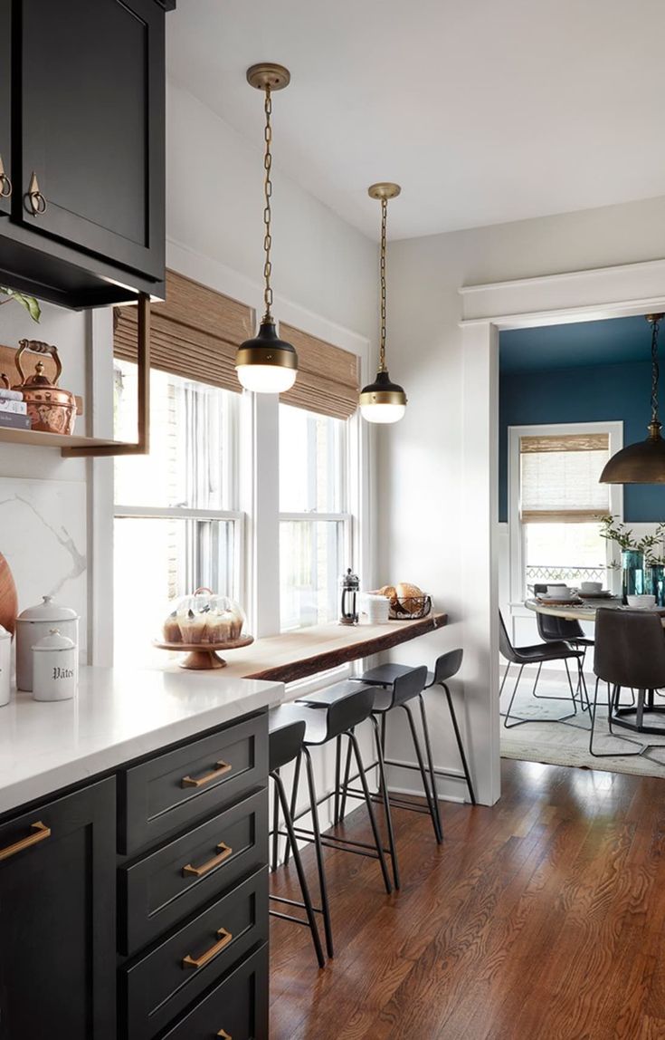 a kitchen with black cabinets and white counter tops next to a dining room table filled with chairs